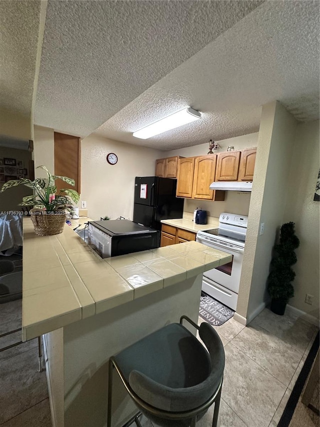 kitchen with black refrigerator, white electric range, tile counters, and a breakfast bar area