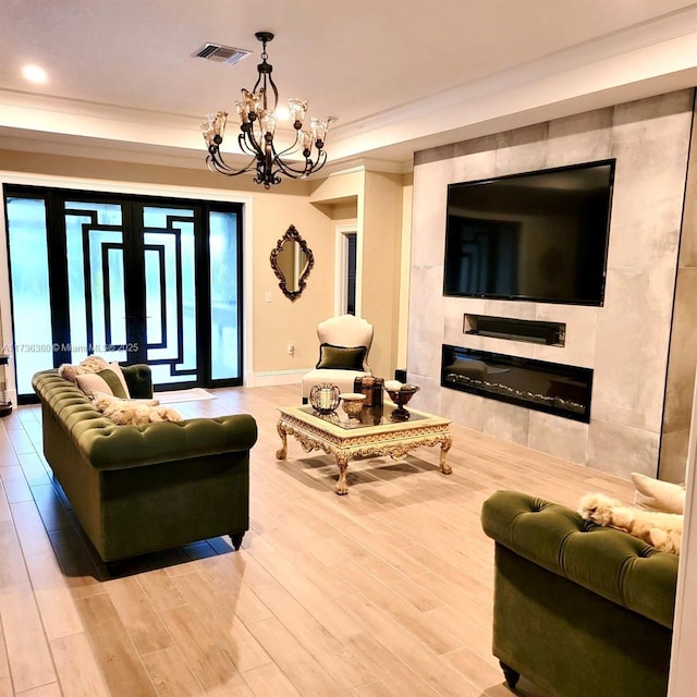 living room with a fireplace, hardwood / wood-style flooring, a notable chandelier, crown molding, and french doors