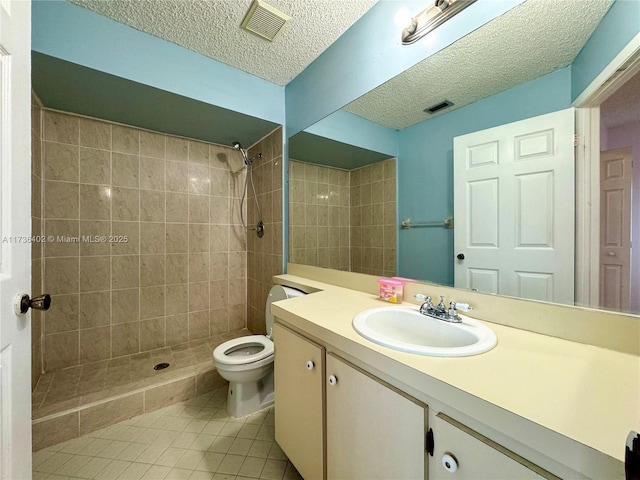 bathroom featuring tile patterned flooring, a tile shower, vanity, a textured ceiling, and toilet