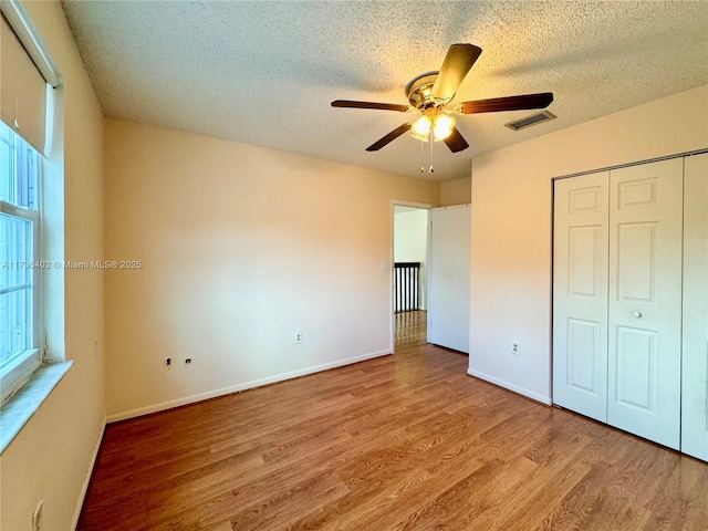 unfurnished bedroom with ceiling fan, a closet, a textured ceiling, and light wood-type flooring