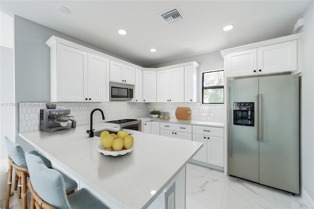 kitchen featuring a breakfast bar area, backsplash, stainless steel appliances, white cabinets, and kitchen peninsula