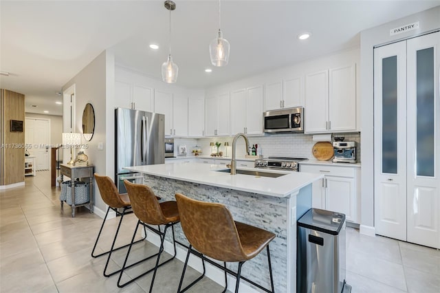 kitchen featuring tasteful backsplash, hanging light fixtures, stainless steel appliances, a kitchen island with sink, and white cabinets