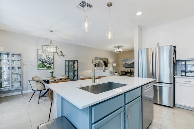 kitchen featuring appliances with stainless steel finishes, pendant lighting, sink, a kitchen island with sink, and blue cabinetry