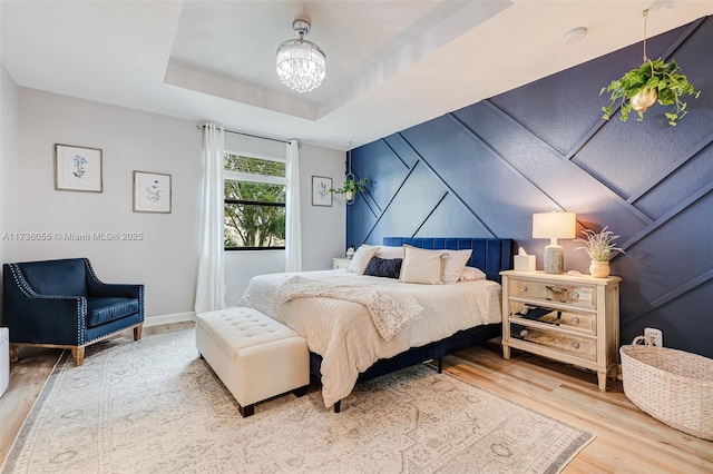 bedroom featuring hardwood / wood-style flooring, a tray ceiling, and a chandelier