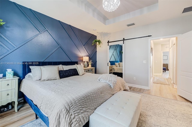 bedroom featuring a tray ceiling, a barn door, a chandelier, and light wood-type flooring