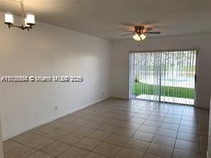 tiled empty room with ceiling fan with notable chandelier