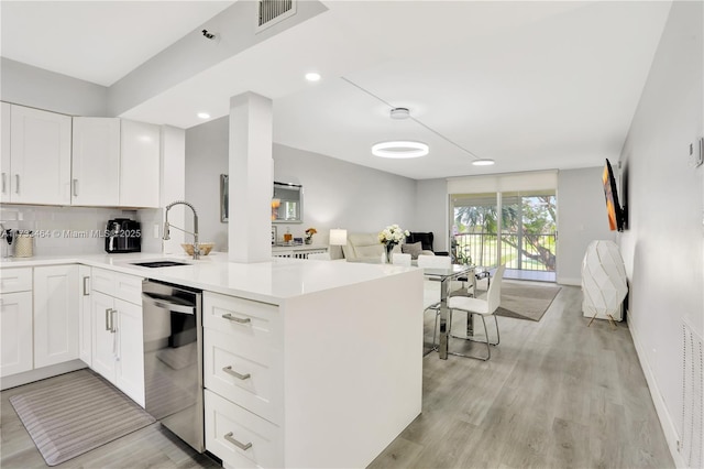 kitchen with sink, white cabinets, decorative backsplash, stainless steel dishwasher, and light hardwood / wood-style flooring