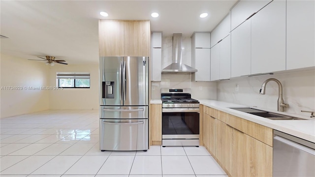 kitchen featuring wall chimney range hood, light tile patterned floors, sink, appliances with stainless steel finishes, and white cabinetry