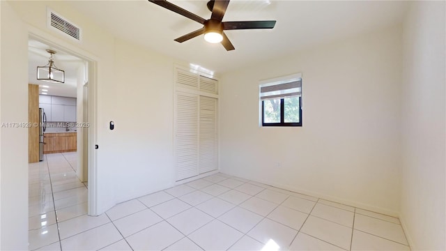 unfurnished bedroom with light tile patterned flooring, ceiling fan, stainless steel fridge, and a closet