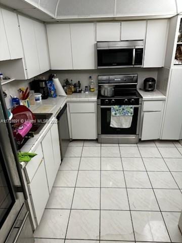 kitchen featuring white cabinets, light tile patterned floors, and black appliances