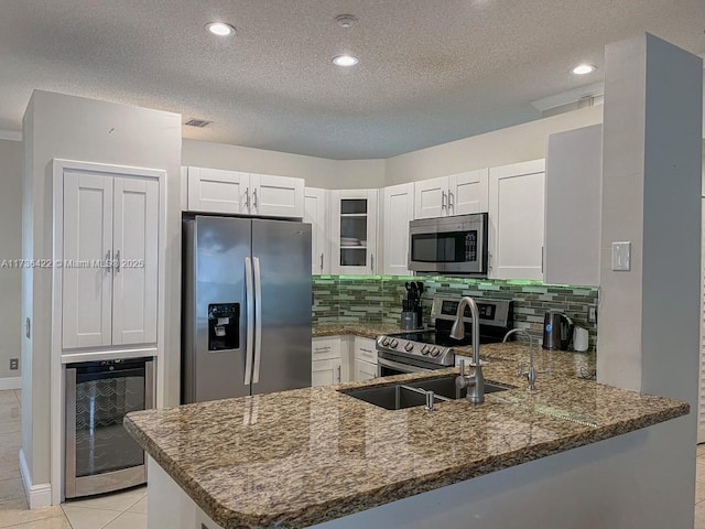 kitchen with wine cooler, stainless steel appliances, a peninsula, dark stone counters, and glass insert cabinets