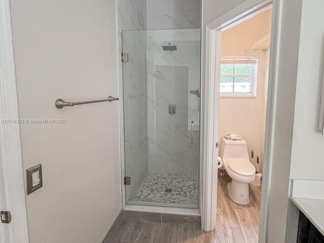 bathroom with toilet, a marble finish shower, and wood finished floors