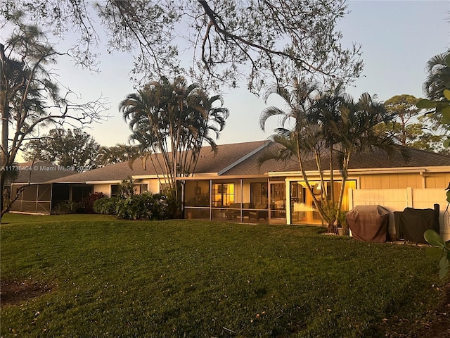 back house at dusk featuring a yard and a sunroom