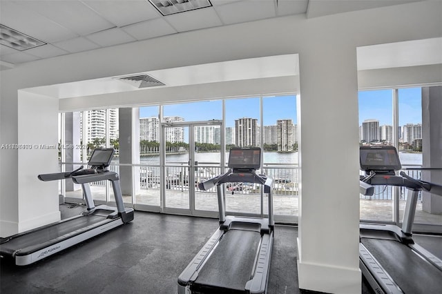 gym with a water view, a paneled ceiling, and a wealth of natural light