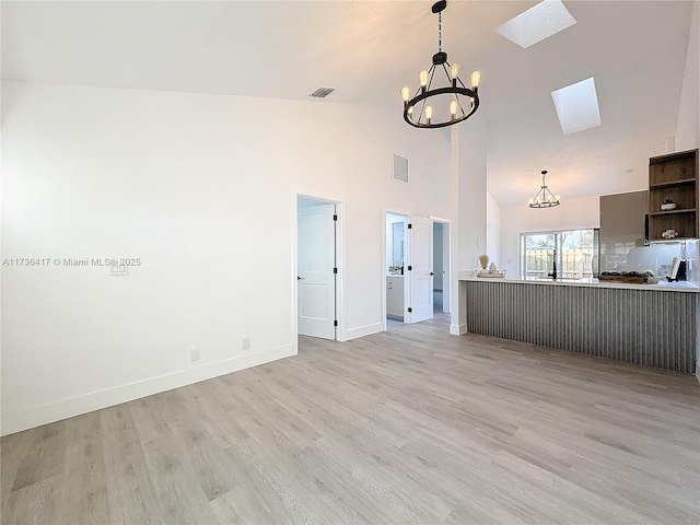 unfurnished living room featuring high vaulted ceiling, a notable chandelier, light hardwood / wood-style floors, and a skylight