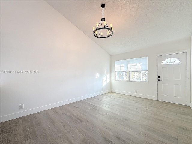 entryway featuring vaulted ceiling, a textured ceiling, an inviting chandelier, and light hardwood / wood-style flooring