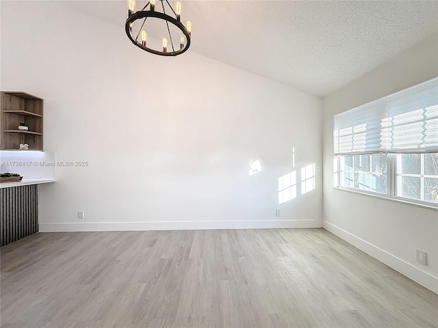 spare room with an inviting chandelier, light hardwood / wood-style floors, and a textured ceiling