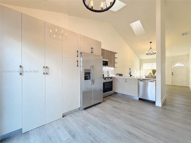 kitchen featuring pendant lighting, a skylight, sink, stainless steel appliances, and light wood-type flooring