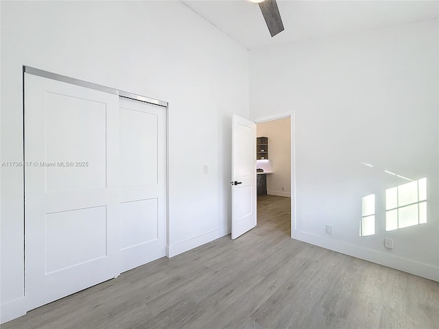 unfurnished bedroom featuring ceiling fan, a towering ceiling, light wood-type flooring, and a closet