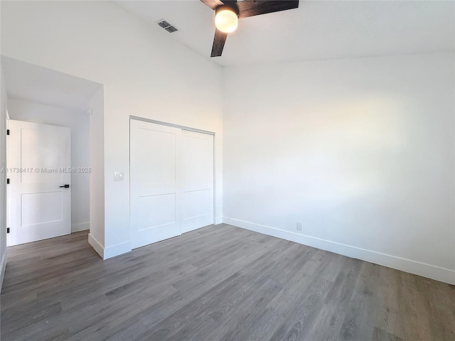 unfurnished bedroom featuring vaulted ceiling, dark wood-type flooring, ceiling fan, and a closet