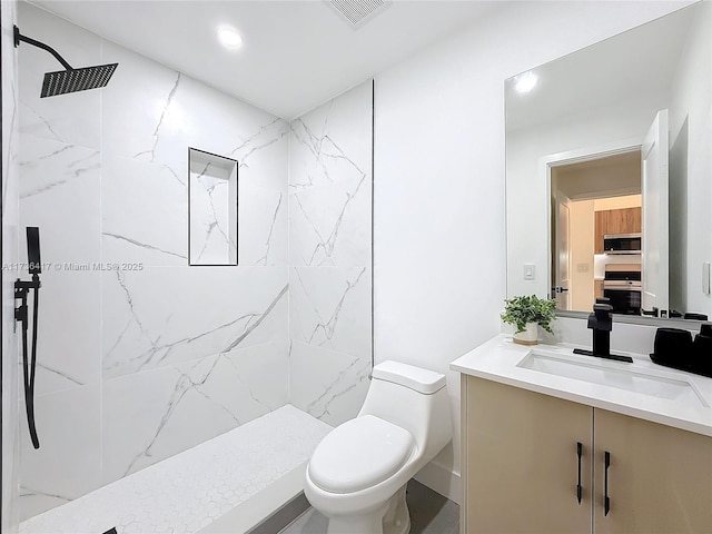 bathroom featuring tiled shower, vanity, and toilet