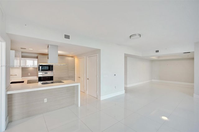 kitchen featuring black microwave, island exhaust hood, stainless steel oven, light tile patterned floors, and kitchen peninsula