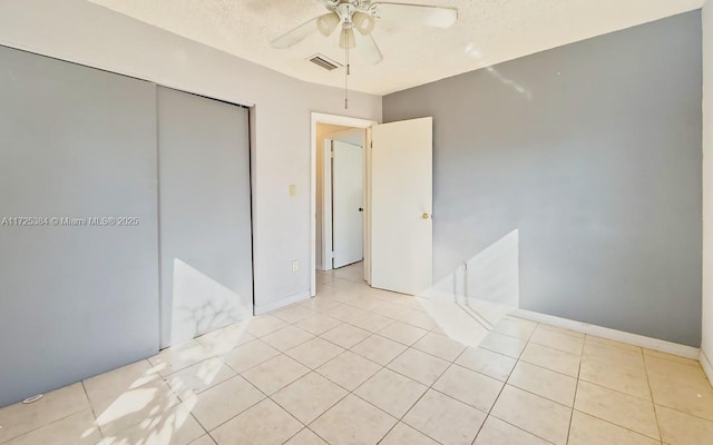 unfurnished bedroom with light tile patterned floors, a textured ceiling, a closet, and ceiling fan