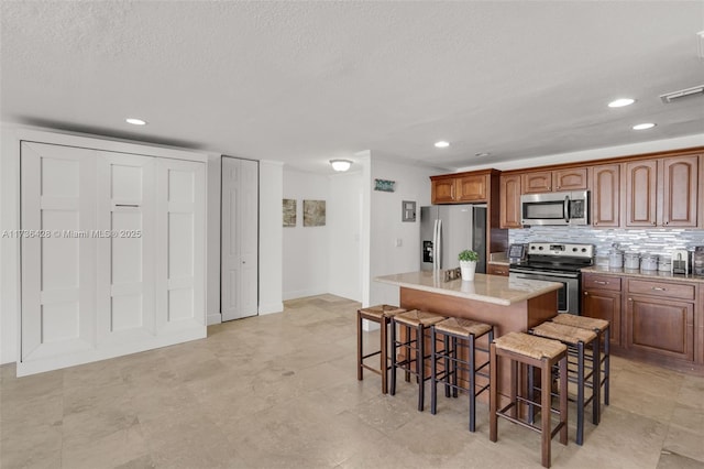 kitchen with backsplash, a breakfast bar area, a textured ceiling, and appliances with stainless steel finishes