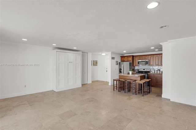 kitchen with crown molding, appliances with stainless steel finishes, backsplash, a center island, and a kitchen bar