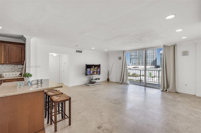 kitchen with floor to ceiling windows, crown molding, light stone counters, a kitchen breakfast bar, and decorative backsplash