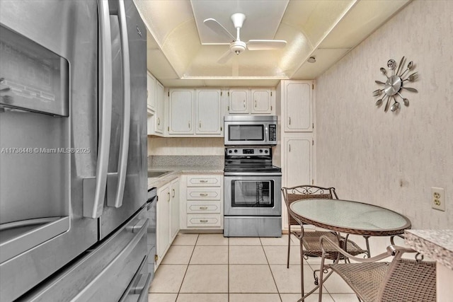 kitchen with ceiling fan, appliances with stainless steel finishes, a tray ceiling, white cabinets, and light tile patterned flooring