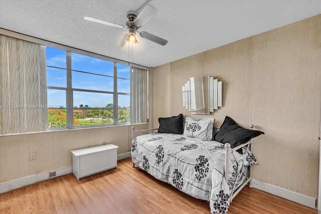 bedroom with ceiling fan, a textured ceiling, and light hardwood / wood-style floors