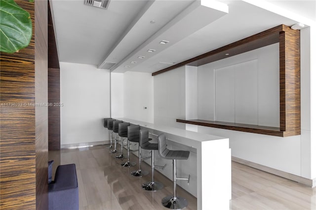 bar with beamed ceiling, light hardwood / wood-style floors, and white cabinets