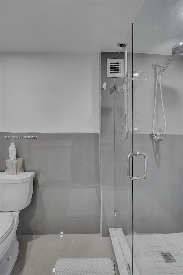 bathroom with tile walls, a shower with shower door, and toilet