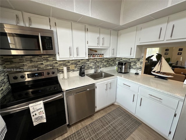 kitchen featuring appliances with stainless steel finishes, white cabinetry, sink, backsplash, and light hardwood / wood-style flooring