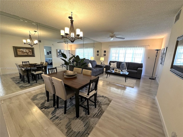 dining space with plenty of natural light, ceiling fan with notable chandelier, a textured ceiling, and light wood-type flooring