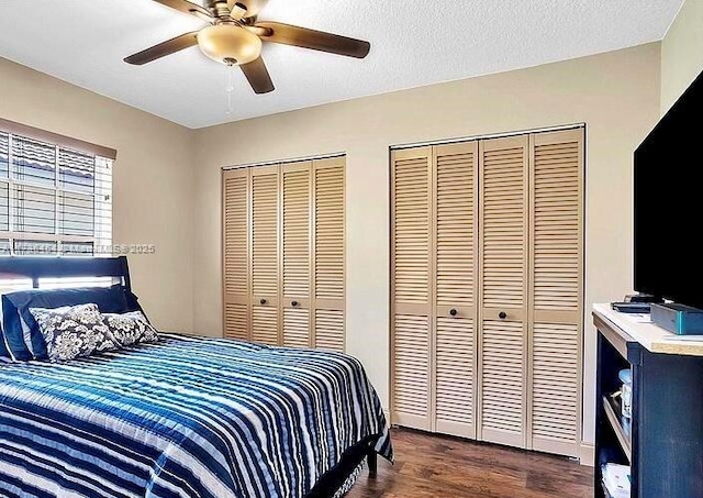 bedroom featuring multiple closets, dark hardwood / wood-style floors, a textured ceiling, and ceiling fan