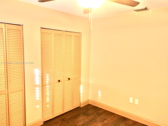 unfurnished bedroom featuring ceiling fan, dark hardwood / wood-style floors, and two closets