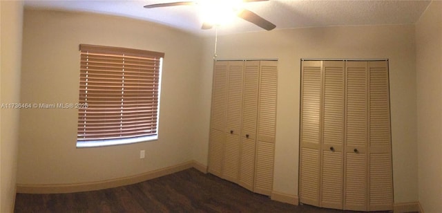 unfurnished bedroom with dark hardwood / wood-style flooring, two closets, and ceiling fan