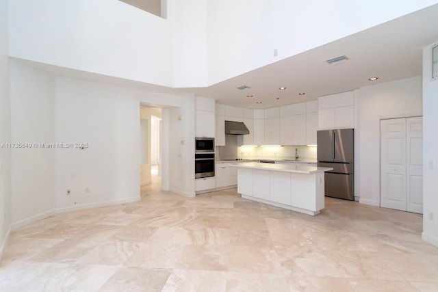 kitchen featuring a kitchen island, appliances with stainless steel finishes, a towering ceiling, sink, and white cabinets