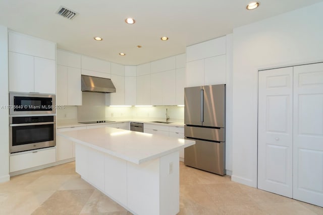 kitchen featuring stainless steel appliances, white cabinetry, a center island, and wall chimney range hood