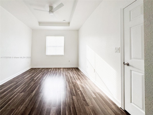 empty room with a raised ceiling, dark hardwood / wood-style floors, and ceiling fan