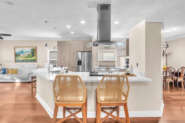 kitchen with a kitchen bar, light hardwood / wood-style flooring, stainless steel fridge, kitchen peninsula, and island exhaust hood