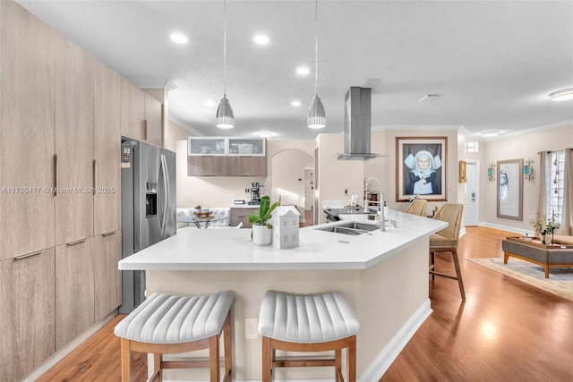 kitchen featuring a breakfast bar, sink, a center island with sink, pendant lighting, and island exhaust hood