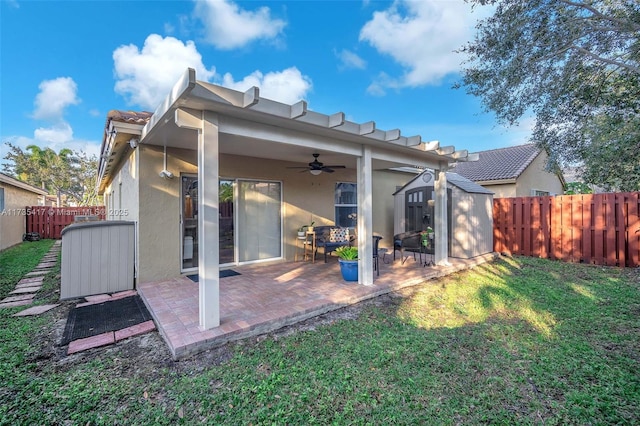 rear view of property featuring ceiling fan, a storage unit, a yard, and a patio