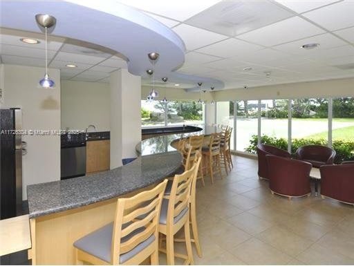 kitchen with pendant lighting, a paneled ceiling, stainless steel dishwasher, and dark stone counters