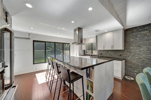 kitchen with white cabinetry, island range hood, a kitchen bar, and dark wood-type flooring