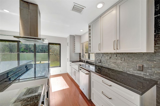 kitchen featuring white cabinetry, stainless steel dishwasher, island range hood, and dark stone countertops