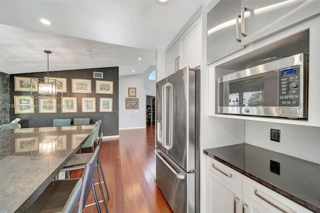 kitchen with white cabinetry, lofted ceiling, dark stone counters, stainless steel appliances, and dark wood-type flooring