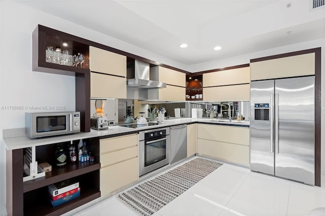 kitchen with sink, light tile patterned floors, appliances with stainless steel finishes, cream cabinets, and wall chimney exhaust hood